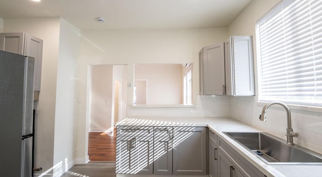 kitchen featuring backsplash, a sink, freestanding refrigerator, and gray cabinetry