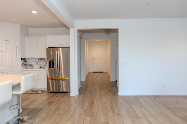 kitchen featuring stainless steel fridge with ice dispenser, light countertops, white cabinetry, light wood-type flooring, and baseboards