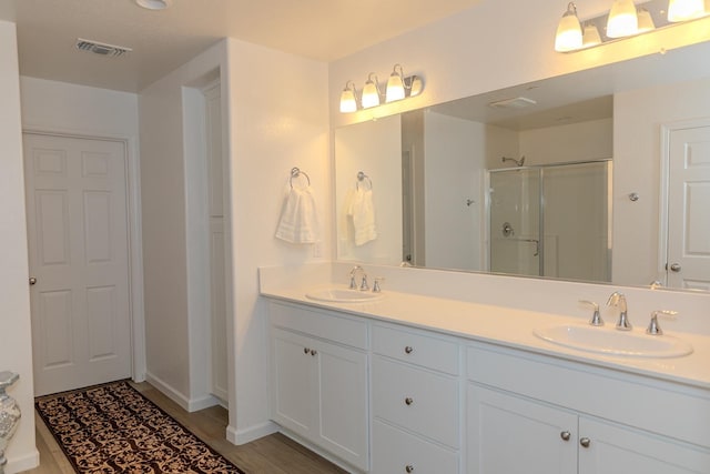 full bath featuring a stall shower, visible vents, a sink, and double vanity