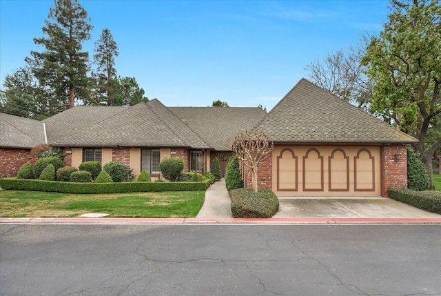 tudor house with concrete driveway, roof with shingles, an attached garage, a front lawn, and brick siding