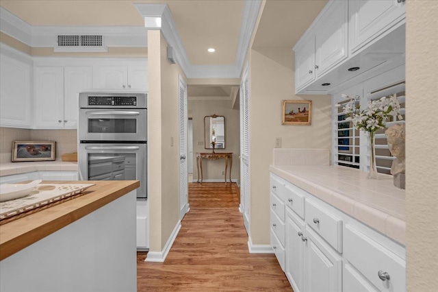 kitchen with visible vents, white cabinets, light wood-style flooring, ornamental molding, and double oven