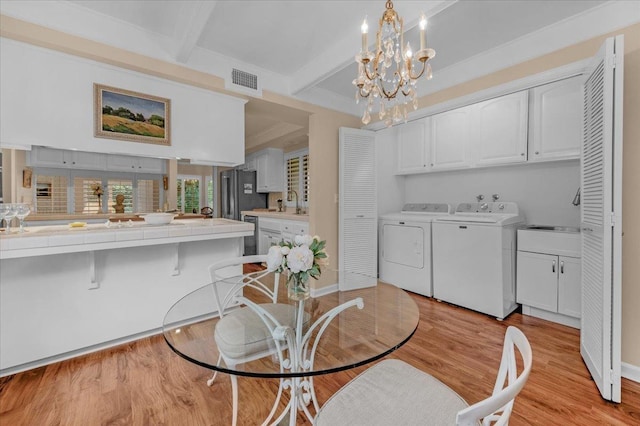 dining space with light wood-style flooring, visible vents, independent washer and dryer, beam ceiling, and an inviting chandelier