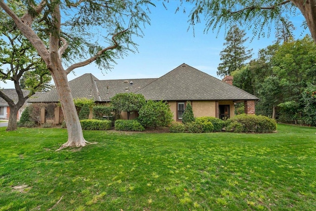 tudor home with a front yard, a chimney, and stucco siding