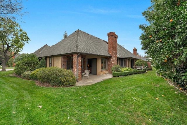 back of property with a patio area, brick siding, a chimney, and a lawn