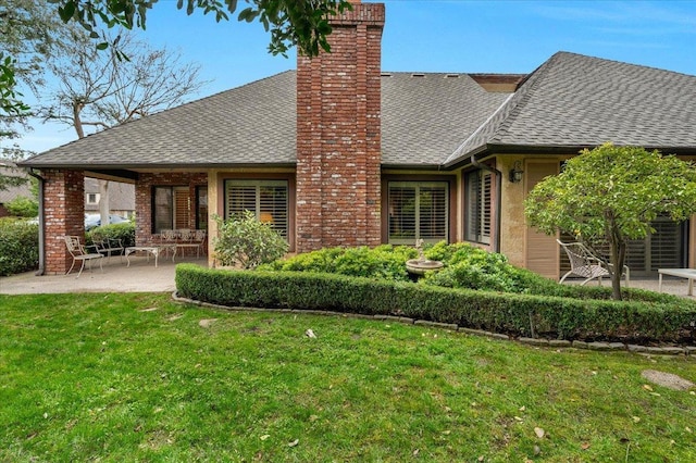 back of property featuring a chimney, roof with shingles, a patio area, and a lawn