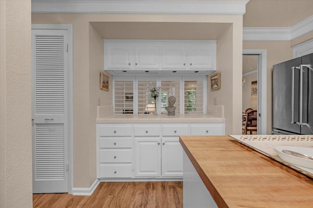 kitchen featuring tile countertops, high end fridge, ornamental molding, white cabinetry, and light wood-type flooring