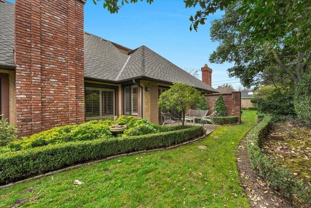 view of side of property featuring a shingled roof, a patio area, a yard, and a chimney