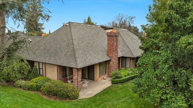 rear view of house featuring a yard, a chimney, a patio area, and roof with shingles