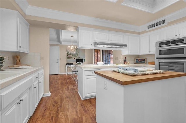 kitchen with visible vents, butcher block counters, wood finished floors, a peninsula, and stainless steel double oven