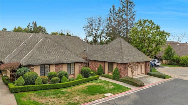 view of front of home with driveway, a shingled roof, an attached garage, a front yard, and brick siding