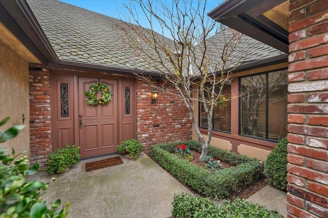 property entrance with a shingled roof and brick siding