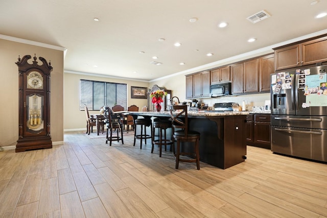 kitchen with crown molding, stainless steel refrigerator with ice dispenser, light wood-style flooring, black microwave, and a kitchen breakfast bar