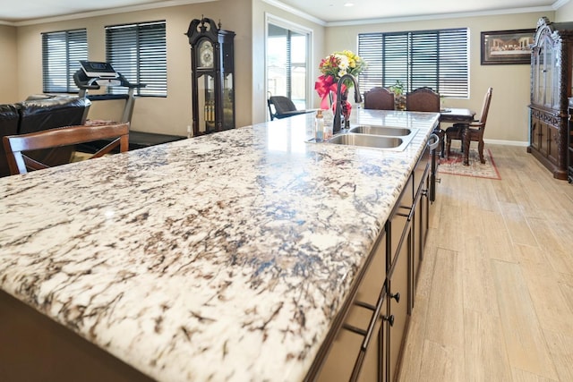 kitchen with light stone counters, open floor plan, crown molding, light wood-style floors, and a sink