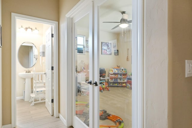 hall featuring light wood-type flooring, baseboards, and french doors