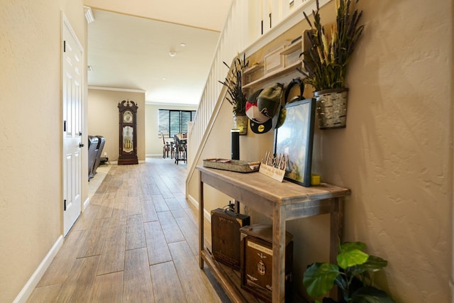 corridor featuring crown molding, baseboards, a textured wall, and light wood finished floors