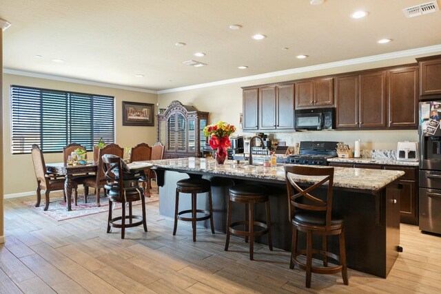 kitchen featuring light wood-type flooring, visible vents, a center island with sink, and black appliances