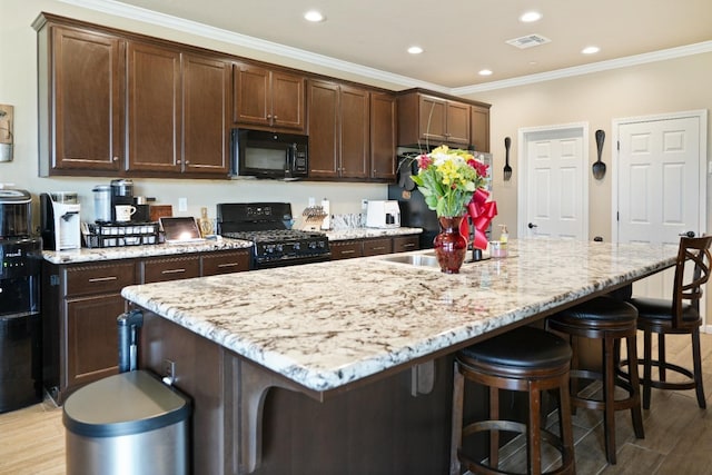 kitchen with visible vents, ornamental molding, a kitchen island with sink, black appliances, and a kitchen bar