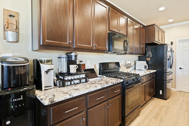 kitchen with light wood-style flooring, light stone counters, crown molding, black appliances, and recessed lighting