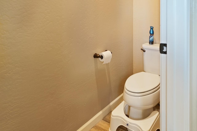 bathroom featuring baseboards, a textured wall, toilet, and wood finished floors