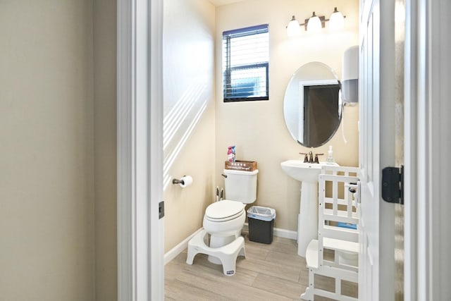 half bathroom with wood finished floors, toilet, and baseboards