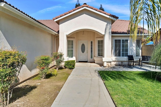 view of exterior entry featuring a tile roof, a patio, a lawn, and stucco siding