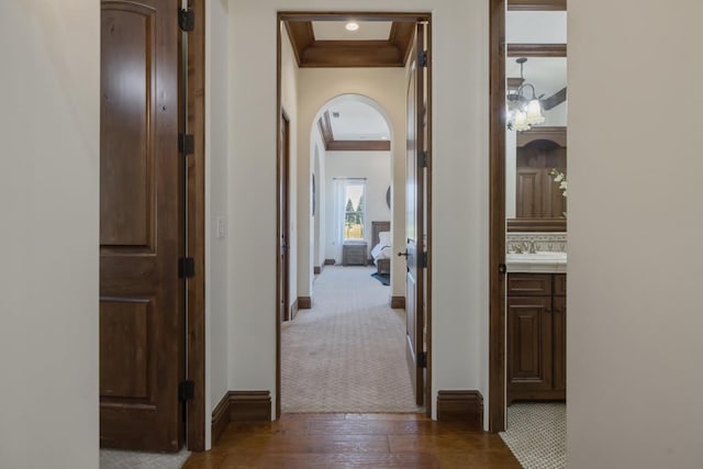 hallway featuring ornamental molding, arched walkways, dark wood-type flooring, and baseboards