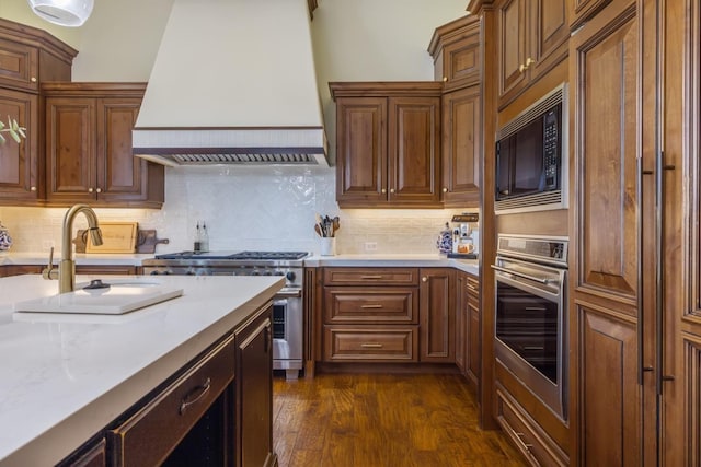 kitchen with dark wood-style floors, appliances with stainless steel finishes, light countertops, premium range hood, and a sink