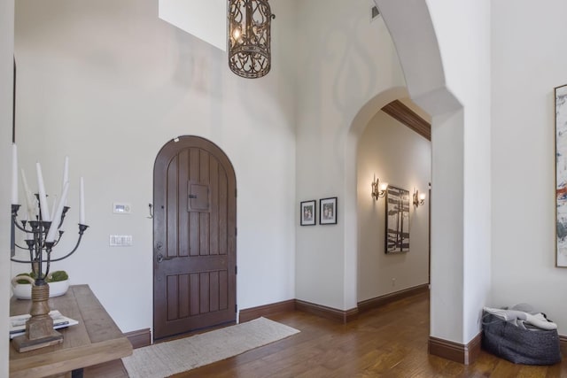 foyer featuring baseboards, a high ceiling, arched walkways, and wood finished floors