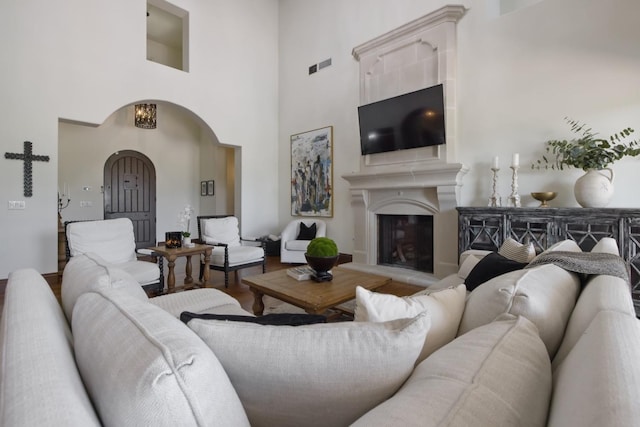 living room featuring arched walkways, visible vents, a high ceiling, a glass covered fireplace, and wood finished floors