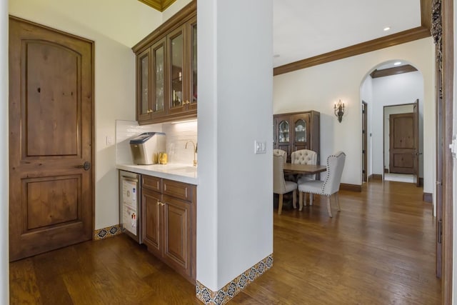 bar with a sink, arched walkways, dark wood finished floors, and backsplash