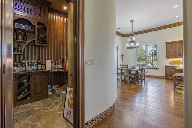 wine room with crown molding, dark wood finished floors, an inviting chandelier, a bar, and baseboards