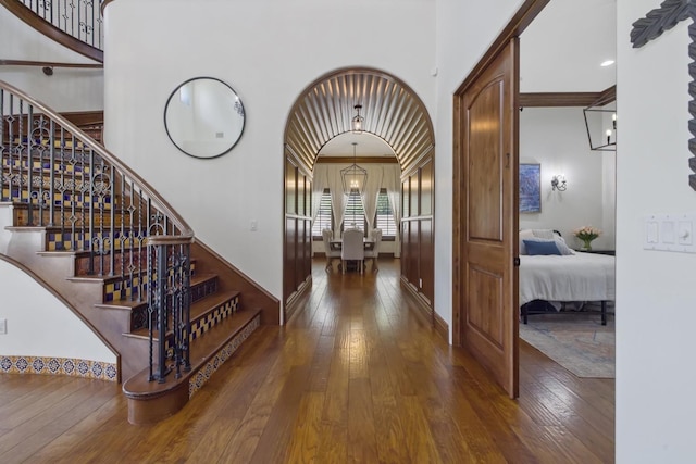 entryway featuring arched walkways, wood-type flooring, a towering ceiling, and baseboards