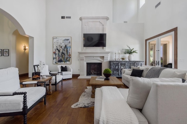 living room featuring arched walkways, a fireplace with raised hearth, dark wood finished floors, and visible vents