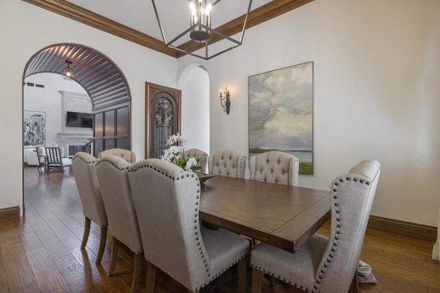 dining area with hardwood / wood-style flooring, a fireplace, arched walkways, and crown molding