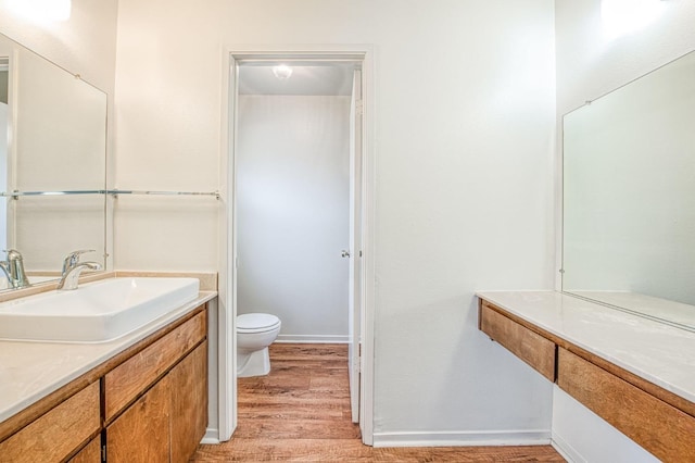 bathroom featuring toilet, baseboards, wood finished floors, and vanity