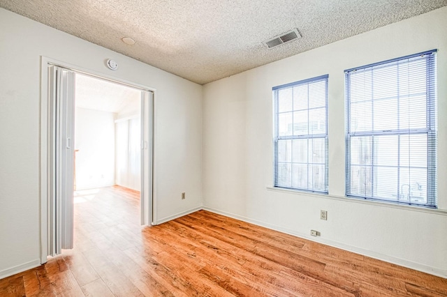 spare room featuring baseboards, visible vents, a textured ceiling, and light wood finished floors