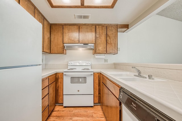 kitchen with white appliances, visible vents, brown cabinets, under cabinet range hood, and a sink