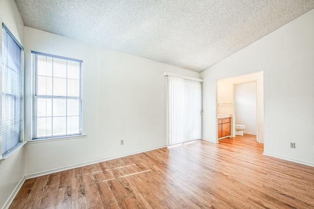 spare room with lofted ceiling, light wood-style flooring, and a textured ceiling