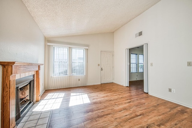 unfurnished living room featuring a fireplace, light wood finished floors, visible vents, vaulted ceiling, and a textured ceiling