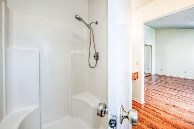 bathroom featuring a textured ceiling, baseboards, walk in shower, and wood finished floors