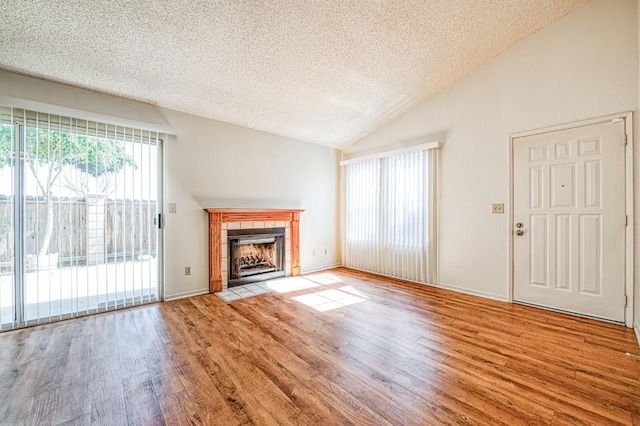 unfurnished living room with a textured ceiling, a fireplace, baseboards, vaulted ceiling, and light wood-style floors