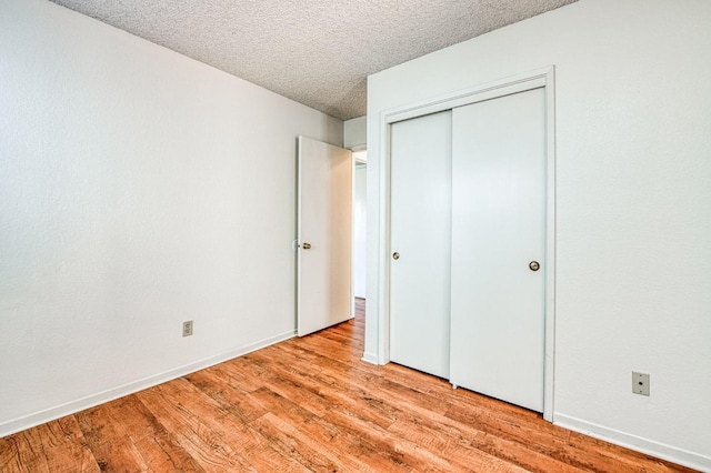 unfurnished bedroom featuring light wood-type flooring, a closet, a textured ceiling, and baseboards