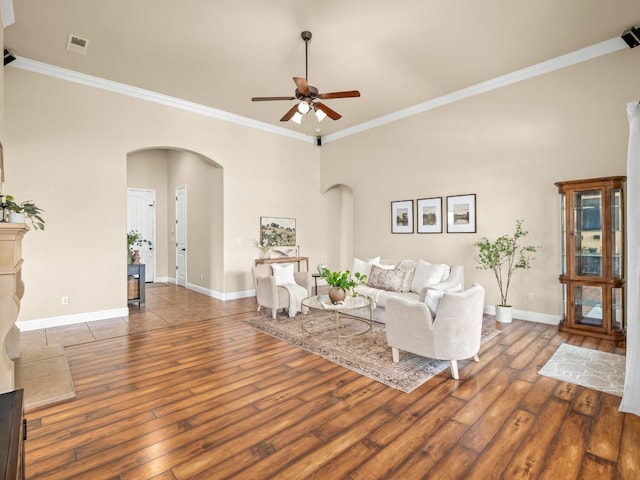 living area featuring arched walkways, crown molding, visible vents, baseboards, and hardwood / wood-style flooring