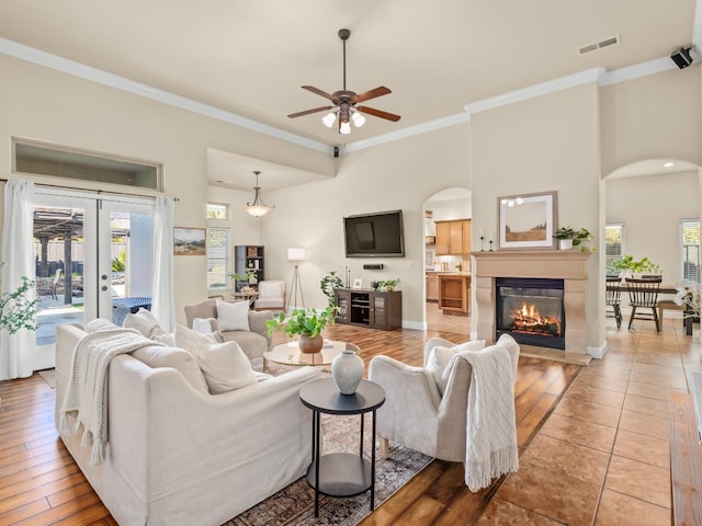 living area featuring visible vents, arched walkways, a glass covered fireplace, crown molding, and french doors