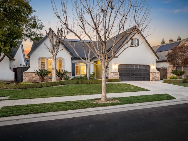 view of front of property with a garage, driveway, a yard, roof mounted solar panels, and stucco siding