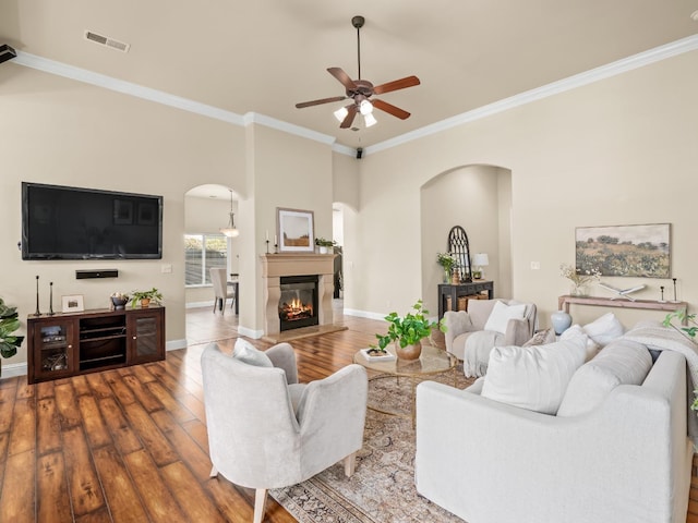 living area with arched walkways, wood finished floors, visible vents, a glass covered fireplace, and crown molding