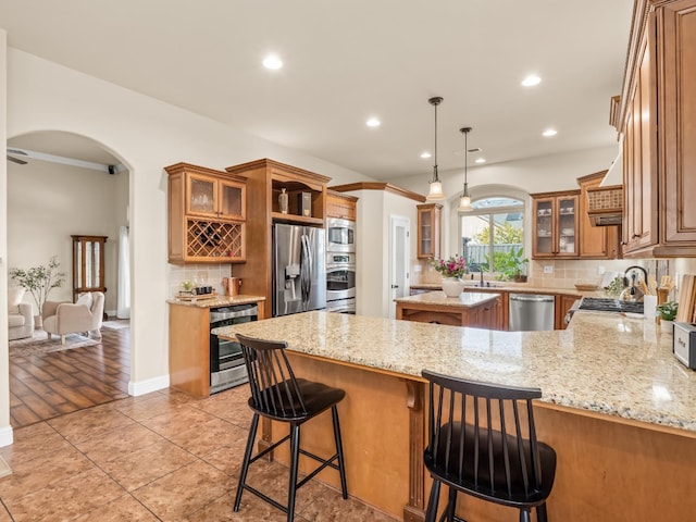 kitchen featuring stainless steel appliances, arched walkways, beverage cooler, and brown cabinetry