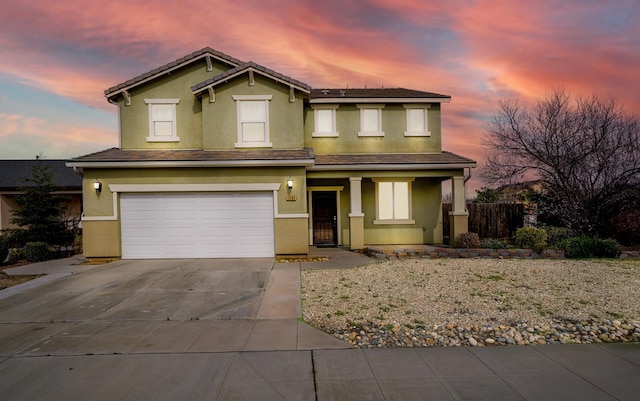 traditional-style house featuring a garage, a tile roof, fence, concrete driveway, and stucco siding