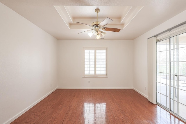 unfurnished room featuring a tray ceiling, a healthy amount of sunlight, baseboards, and wood finished floors