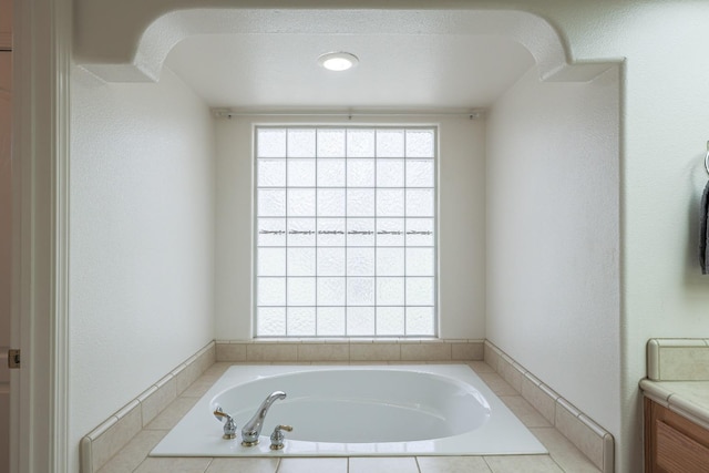 full bathroom with a wealth of natural light, a textured wall, vanity, and a bath